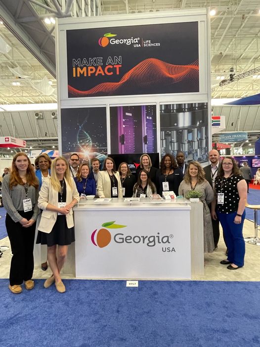 A group of BIO International Conference attendees stand and pose around the Georgia USA booth at the conference.