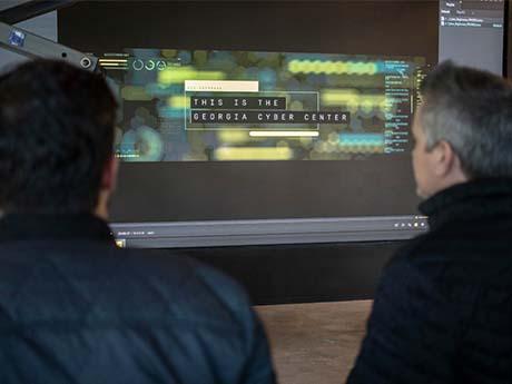 two people look at a screen that says "This is the Georgia Cyber Center"