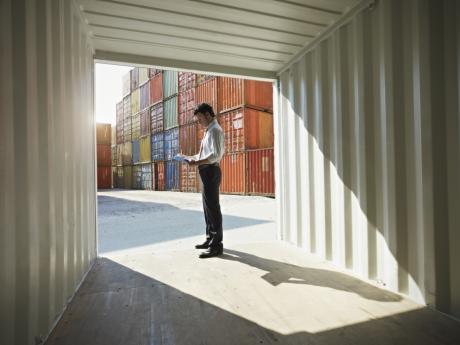 man stands in front of shipping containers and looks at paper